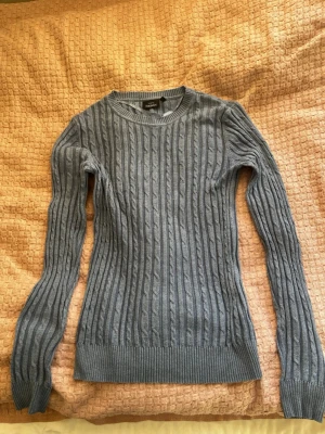 Blå kabelstickad tröja - Snygg blå kabelstickad tröja från Gina Tricot med rund halsringning och långa ärmar. Tröjan har ribbade muddar vid ärmslut och nederkanten. Perfekt för en kyligare vår/sommarkväll. 