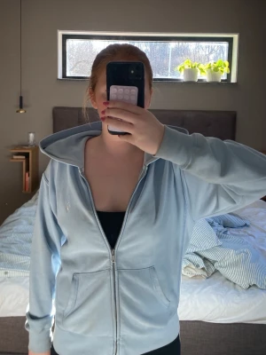 Ljusblå hoodie från Polo Ralph Lauren - Ljusblå hoodie med dragkedja från Polo Ralph Lauren. Klassisk design med huva, två fickor framtill och broderad logga på bröstet. Tillverkad i mjukt material som känns skönt mot huden. Perfekt för en avslappnad och stilren look.