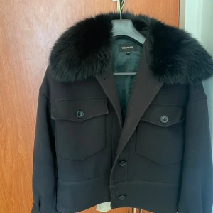 Svart jacka från Meotine - Stilren svart jacka från Meotine med stor, fluffig krage. Jackan har två stora bröstfickor med knappar. Inga skador och inget fel på den. Köpt för 3900.