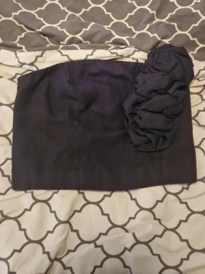 Svart oneshoulder tubtopp med volang - Sny trade;gg svart oneshoulder disappeared tubtopp med stor volangdetalj intens på axeln. Toppen är axelbandslös och har en elastisk panel på baks/des för Wie bättre passform. Perfekt för dig som vill sticka ut med en unik topp.