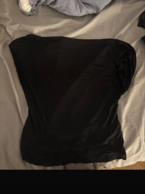 Svart topp utan rygg  - Säljer en svart topp utan rygg i mjukt material. Toppen har en enkel och stilren design utan synliga detaljer eller mönster, perfekt för att matcha med olika outfits. Passformen är normal och tyget känns lätt och bekvämt.