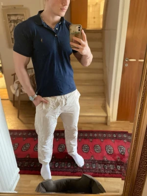 Marinblå piké från Polo Ralph Lauren - Säljer en marinblå pikétröja från Polo Ralph Lauren i slim fit. Klassisk design med korta ärmar, krage och knappar framtill. Tillverkad i mjuk bomull och har den ikoniska loggan broderad på bröstet.