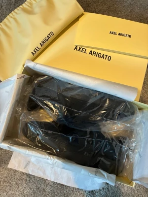 Svarta sneakers från Axel Arigato - Snygga svarta sneakers från Axel Arigato i minimalistisk design. Skorna har en stilren siluett och är tillverkade i slätt läder. Levereras i originalkartong med dustbag och tillbehör. Perfekta för dig som gillar trendiga och klassiska sneakers.