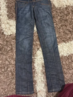 Mörkblå raka jeans med dubbla knappar - Säljer ett par mörkblå jeans med raka ben och snygga kontrastsömmar. Jeansen har dubbla knappar i midjan och klassiska fem fickor. Materialet är denim i bomull och passformen är avslappnad men ändå stilren.