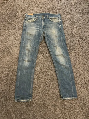Dondup - Säljer ett par blå smala jeans från Dondup med slitna detaljer och klassisk femficksmodell. Jeansen har en snygg tvätt med ljusa partier och är tillverkade i bomull. Perfekta för dig som gillar en avslappnad men trendig stil.