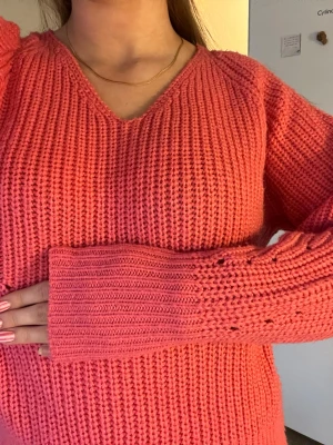 Koralrosa stickad tröja med v-ringning - Säljer en korallrosa stickad tröja med v-ringad hals och långa ärmar. Tröjan har breda ribbade muddar och är gjord i ett grovt stickat material som känns mjukt och skönt. Perfekt att matcha med jeans för en avslappnad look.