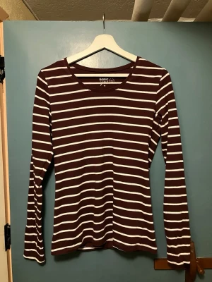 Randig vinröd långärmad topp  - Säljer en långärmad topp från Basic You/Ullared i vinrött och vitt med klassiskt randigt mönster. Tillverkad i mjuk ekologisk bomull som känns skön mot huden. Perfekt till jeans eller kjol för en enkel och snygg look.