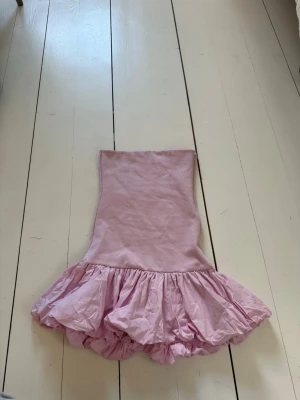 Ljusrosa axelbandslös volangklänning - Supersöt ljusrosa kort klänning med volangkjol och axelbandslös design.