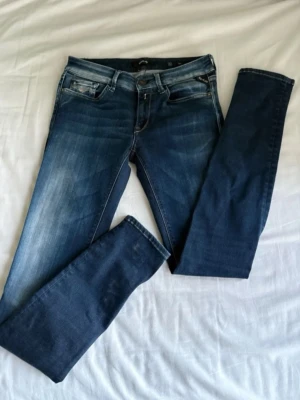 Mörkblå skinny jeans med slitningar - Säljer ett par mörkblå skinny jeans med snygga slitningar och tvättade detaljer. Jeansen har fem fickor, låg midja och smala ben. Materialet är stretchigt denim som sitter tajt och bekvämt. Perfekta för en trendig och avslappnad look.