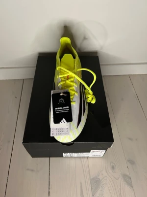 Adidas F50 gula fotbollsskor AG - Säljer ett  par helt nya F50 för konstgräs i neon-gult med vita och svarta detaljer. Skorna har snörning och en modern, strömlinjeformad design. Tillverkade i syntetmaterial för bästa prestanda på planen. Perfekta för dig som vill sticka ut!