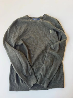 Grön stickad tröja Polo Ralph Lauren - Mörkgrön stickad tröja från Polo Ralph Lauren i slim fit-modell. Tillverkad i mjuk och tvättbar merinoull med rund halsringning och diskret broderad logga på bröstet. Skriv ifall du har frågor!