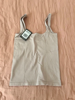 Beige ribbat linne från Aimn - Beige linne från Aimn med ribbad struktur och breda axelband. Tillverkat i ett stretchigt material som sitter skönt mot kroppen. Enkel och stilren design, perfekt för träning eller som basplagg.