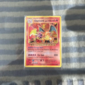 Charizard Pokémonkort Base Set - Säljer ett Charizard Pokémonkort från Base Set med 150 HP och Fire Spin-attack. Kortet har en röd och gul design med Charizard i mitten och är tillverkat av laminerad kartong. Perfekt för samlare eller Pokémonfans som vill ha en ikonisk figur i sin samling.