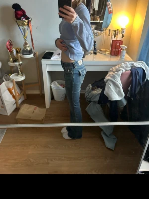True Religion  - Säljer ett par blå bootcut jeans från BECCA med mid-rise passform. Jeansen har klassiska fickor och snygga kontrastsömmar. Perfekt för dig som gillar en avslappnad och trendig look. Materialet är denim och de har en bekväm passform.