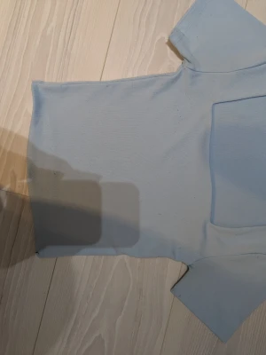 Ljusblå topp från Amisu - Snygg ljusblå topp från Amisu med korta ärmar och enkel, stilren design. Tillverkad i ett mjukt och stretchigt material som sitter bekvämt. Perfekt att matcha med jeans eller kjol för en clean look. Toppen är nopprig som syns på bilderna men syns knappt på, visas på sista bilden.