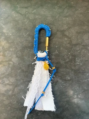 Blå och vit väskdekoration - Unik väskdekoration med blått snöre, guldiga detaljer och denim i vitt tyg. Karbinhake insvept i blå tråd och en liten guldfärgad berlock. Perfekt för att ge din väska en personlig touch.