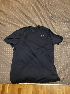 Svart Nike Dri-Fit t-shirt - Säljer en svart Nike Dri-Fit t-shirt med klassisk vit Swoosh-logga på bröstet. Tillverkad i ett lätt och snabbtorkande funktionsmaterial som passar perfekt till träning eller sport. Enkel och stilren design med rund hals och korta ärmar.
