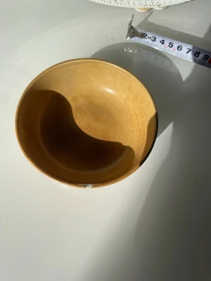 Duka Terra skål - Säljer en rund skål i keramik med varm brun färg och glaserad yta. Skålen har en diameter på cirka 13 cm och passar perfekt till snacks, frukt eller småprylar. Enkel och stilren design som ger en retrovibe till hemmet.