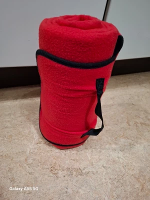 Röd fleecefilt med bärhandtag - Mysig röd fleecefilt med svarta kanter och praktiskt bärhandtag. Perfekt att ta med till picknick, stranden eller på resan. Filten är lätt att rulla ihop och smidig att bära med sig tack vare handtaget.