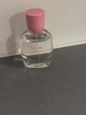 Orchid Zara parfym med rosa kork - Fräsch parfym från Zara i serien Orchid. Flaskan är genomskinlig med rund form och har en söt rosa kork. Texten på flaskan är i rosa och vitt. Perfekt för dig som gillar blommiga och feminina dofter.