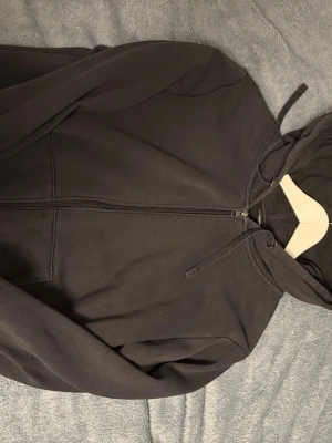 Svart zip hoodie med huva - En enkel och stilren svart hoodie med dragkedja framtill och justerbar huva. Hoodien har långa ärmar och två fickor på sidorna. Tillverkad i mjukt sweatshirtmaterial som är skönt mot huden. Perfekt för en avslappnad look.