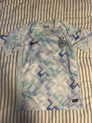 Inter Milan matchtröja blåvit Nike  - Säljer en Inter Milan matchtröja från Nike i vitt med ljusblått och blått pixelmönster. Tröjan har korta ärmar, rund hals och klubbmärke samt Nike-logga på bröstet. Tillverkad i ett lätt och ventilerande material, perfekt för fotboll eller träning.