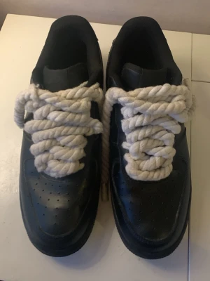 Svarta sneakers med grova snören - Unika svarta sneakers i läder-look med riktigt grova, vita rep som skosnören. Klassisk låg modell med perforerade detaljer på tån och rundad tå. Perfekt för dig som vill sticka ut med din stil.