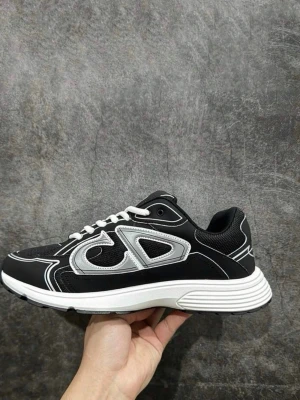 Svarta sneakers med vit sula och detaljer - Snygga svarta sneakers med vit sula och vita samt silverfärgade detaljer. Skon har en sportig design med mesh och syntetmaterial, samt vita skosnören. Perfekt för dig som gillar streetwear och vill ha en modern look.