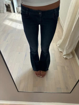 Mörkblå bootcut jeans - Snygga mörkblå bootcut jeans med låg midja och klassisk femficksdesign. Jeansen har en lätt utsvängd passform nedtill och stängs med knapp och dragkedja. Perfekta för en trendig och avslappnad look. Utsydda i benen 