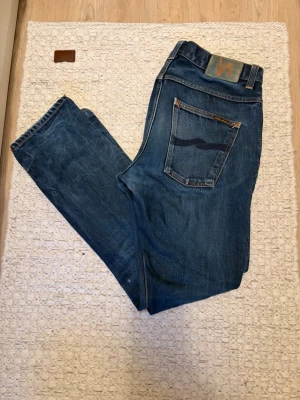 Blå jeans från Nudie Jeans -  Säljer ett par jättecoola Nudie Jeans (Dude Dan, Dry Midnight) i mörkblå tvätt med orangea sömmar, knappgylf och snygg vintage wash slitning . 100% ekologisk bomull. Använt men bra skick, finns ett litet slitet parti i grenen som går lätt att laga (se sista bilden). Moving, price can be discussed if you buy fast! ⚡️ Rensar ut allt, samfraktar gärna. Fraktar direkt! 📦✨
