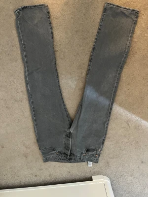Grå raka jeans - Säljer ett par grå jeans med rak passform och hög midja. Jeansen har klassiska fem fickor och knappgylf. Materialet är denim i bomull och färgen är en snygg tvättad grå. Perfekta till en avslappnad look.
