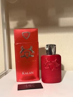 Kalan parfym från Parfums de Marly - Kalan är en exklusiv parfym i en matt röd flaska med silverfärgat lock och reliefmönster med två hästar och sköld. Flaskan rymmer 125 ml och kommer i en matchande röd kartong med silverdetaljer. Doften är intensiv och elegant, perfekt för dig som gillar lyxiga parfymer.