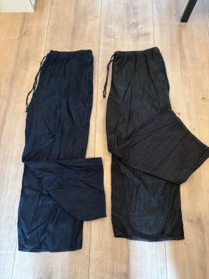 Mörkblå loose fit jeans med dragsko - Två par mörkblå jeans med avslappnad passform och dragsko i midjan. Byxorna har raka ben och är tillverkade i ett mjukt denimtyg som ger en chill och bekväm känsla. Perfekta för dig som gillar en ledig stil och vill ha extra rörelsefrihet. Mörkblåa endast använd 3 gånger och svarta 1 gång, som nya. Ord pris per byxa 349kr