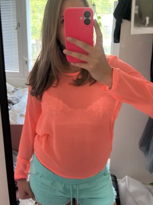 Korall ångärmad blus - Säljer en korall långärmad blus med transparent material och rund halsringning. Toppen är lätt och luftig, perfekt för att sticka ut med en färgstark look. Passar dig som gillar att synas och vill ha något unikt i garderoben.