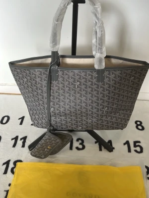 Grå G handväska med mönster - Snygg grå handväska från G med det klassiska vita mönstret och matchande liten clutch. Väskan har två handtag och är tillverkad i canvas med läderdetaljer. Perfekt för dig som vill ha en trendig och rymlig väska med exklusiv känsla.