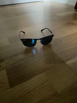 Ray-Ban solglasögon - Snygga mörblåa solglasögon från Ray-Ban med klassisk halvbågsform och spegelblå linser. Metallbågarna ger en stilren look och loggan syns tydligt på linsen. Perfekta för soliga dagar och ger en cool vibe. Jag har tyvärr tappt bort fodralet men man får med ett annat som funkar perfekt. Ny pris runt 2000kr.                                                Kom med bud