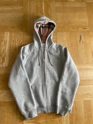 Grå zip hoodie från Burberry - Grå zip hoodie från Burberry med klassiskt rutigt foder i huvan. 