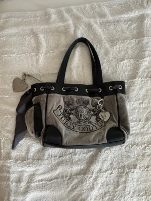 Juicy Couture väska - Vintage grå juicy couture väska. Den är i jättefint skick och har inga defekter. Köpt på vestiaire och har äkthetsintyg. Säljer då den inte kommer till användning🩶