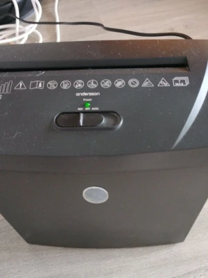 Svart dokumentförstörare Andersson - Elektrisk dokumentförstörare från Andersson i svart plast. Utrustad med strömbrytare och indikatorlampa, samt tydliga symboler för säker användning. Har en avtagbar behållare för pappersavfall och ansluts med vanlig elkabel.