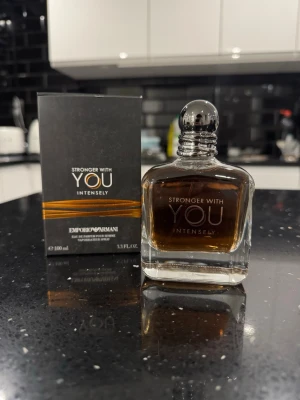 Armani Stronger With You Intensely  - Stronger With You Intensely från Emporio Armani är en elegant parfym i en stilren, fyrkantig glasflaska med silverfärgad kork. Doften har en djup bärnstensfärg och flaskan rymmer 100 ml. Förpackningen är svart med guldiga detaljer.