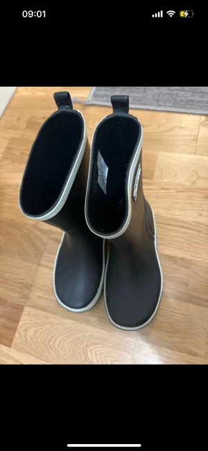 Svarta gummistövlar från Trekmates - Säljer ett par svarta gummistövlar från Trekmates med vit kant upptill och längs sulan. Klassisk hög modell med dragflik bak för enkel påtagning. Perfekta för regniga dagar och festivaler. Tillverkade i slitstarkt gummi.