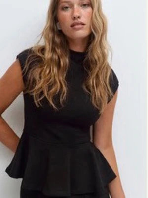 Svart peplum topp med hög hals - Trendig svart peplum topp med hög hals och korta ärmar. Toppen har en markerad midja och volang nedtill som ger en snygg siluett. Perfekt att styla med både jeans och kjol för en cool look.