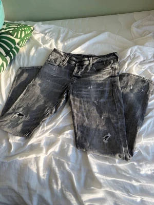 Jack & Jones jeans - Säljer ett par grå jeans med slitningar och hål på både lår och knän. Jeansen har klassisk femficksmodell, raka ben och en cool, tvättad look. Perfekta för dig som gillar en avslappnad och trendig stil.