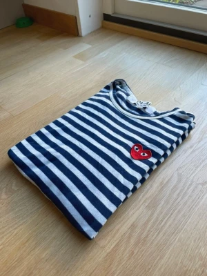 Randig Comme des Garçons longsleeve - Perfekt klassisk randig långärmad från Comme des Garçons PLAY i storlek M. Ikoniska röda hjärtloggan fram. Äkta vara med originaltaggar (se bilder). Skicket är mycket bra - inga fläckar, hål eller tvättslitage.  Nypris ligger runt 1500-2000 kr, så detta är ett riktigt bra kap. Den är liten i storleken!!! Jag gör inte returer så kolla måtten noga innan köp!!!!! Tvättlappen är avklippt (se sista bild) men annars är den i topp skick!