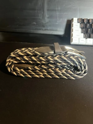 Flätat bälte - Snyggt flätat bälte i svart och vitt med silverfärgat spänne. Bältet har en cool randig look och detaljer i svart skinn vid spännet. Perfekt accessoar för att lyfta din outfit.