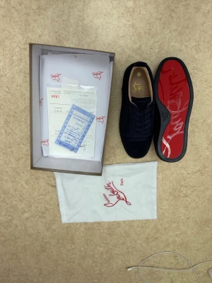 Mörkblå sneakers från Louboutin - Snygga mörkblå sneakers från Christian Louboutin i mocka med klassisk röd sula och gulddetaljer på innersulan. Skorna har lågt skaft, rund tå och matchande mörkblå snörning. Kommer med originalkartong och dustbag.