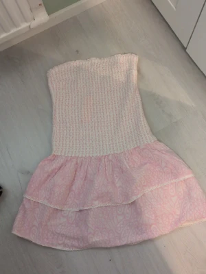 Söt rosa volangklänning - Supersöt kort klänning i ljusrosa med smock upptill och dubbla volanger nertill. Klänningen är axelbandslös och har ett diskret mönster i tyget. Perfekt för varma dagar och ger en romantisk vibe. Ge gärna prisförslag ☺️