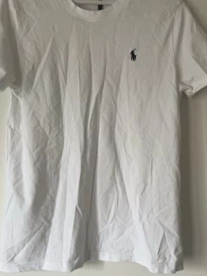 Ralph lauren Vit t-shirt med liten logga - Klassisk Ralph lauren  vit t-shirt med rund hals och liten broderad logga på bröstet. T-shirten är kortärmad och tillverkad i mjuk bomull, perfekt för en clean och enkel stil.
