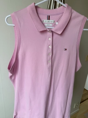 Ljusrosa ärmlös pikétopp Tommy Hilfiger - Snygg ljusrosa ärmlös pikétopp från Tommy Hilfiger med klassisk krage och knappar framtill. Liten logga broderad på bröstet. Perfekt till sommaren och enkel att matcha med jeans eller kjol.