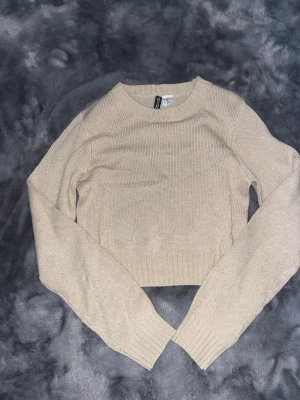 Beige cropped stickad tröja - Snygg beige stickad tröja med croppad passform och långa ärmar. Tröjan har rund halsringning och ribbade muddar vid ärmslut och nederkant. 
